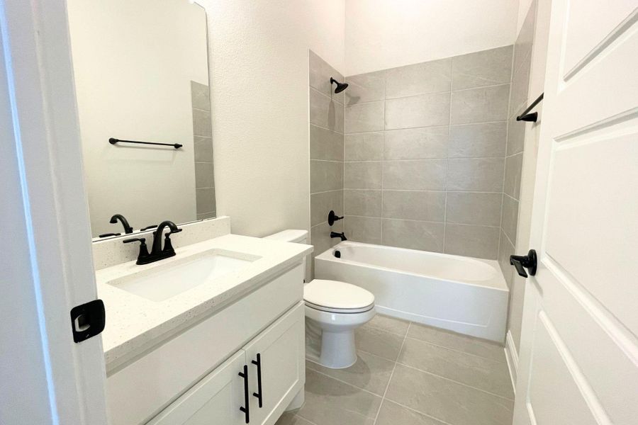 Tiled flooring, clean quartz vanities, and modern black fixtures complete this classic bathroom space. Tiled flooring, clean quartz vanities, and modern black fixtures complete this classic bathroom space.