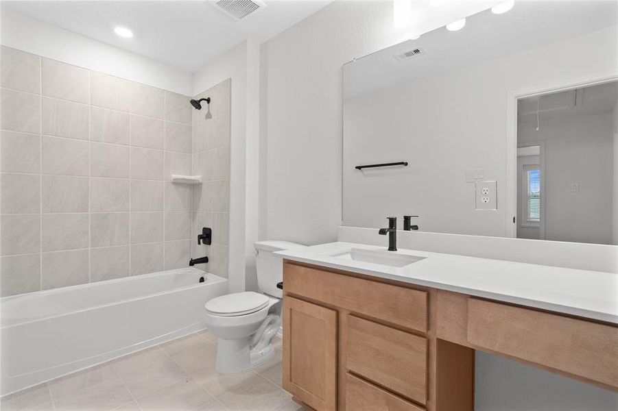 Secondary bath features tile flooring, bath/shower combo with tile surround, stained wood cabinets, beautiful light countertops, mirror, sleek fixtures and modern finishes.