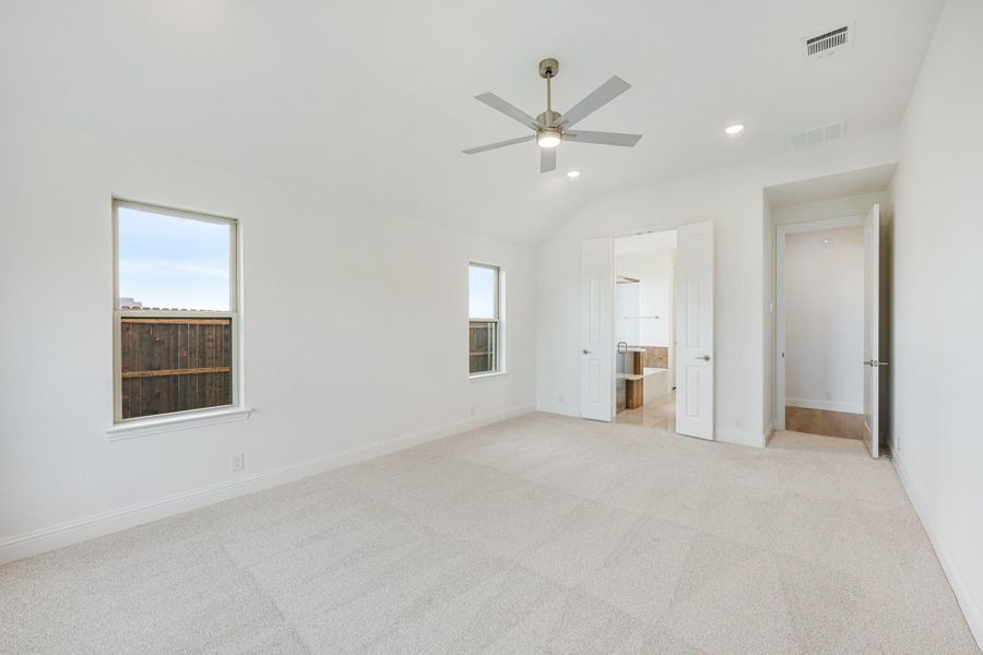 Empty bedroom with vaulted ceiling, ceiling fan, carpet flooring, and doorway leading to ensuite bathroom Empty bedroom with vaulted ceiling, ceiling fan, carpet flooring, and doorway leading to ensuite bathroom