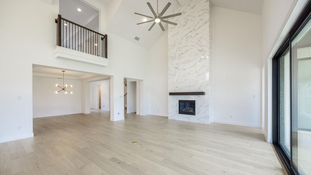 Unfurnished living room featuring high vaulted ceiling, light wood-style floors, a fireplace, a ceiling fan, and a chandelier Unfurnished living room featuring high vaulted ceiling, light wood-style floors, a fireplace, a ceiling fan, and a chandelier