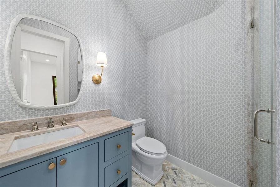 The bathroom features a vanity with a light-colored countertop and a vessel sink, a wall-mounted light fixture, and patterned wallpaper