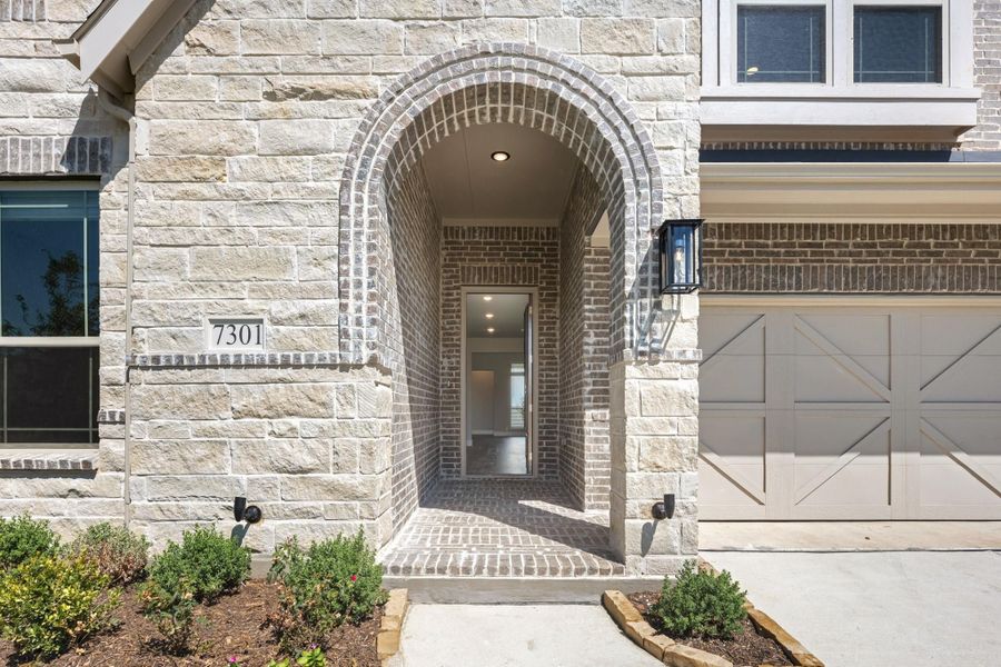 Home entrance with arched brick doorway, stone exterior, and attached garage at address 7301 Home entrance with arched brick doorway, stone exterior, and attached garage at address 7301