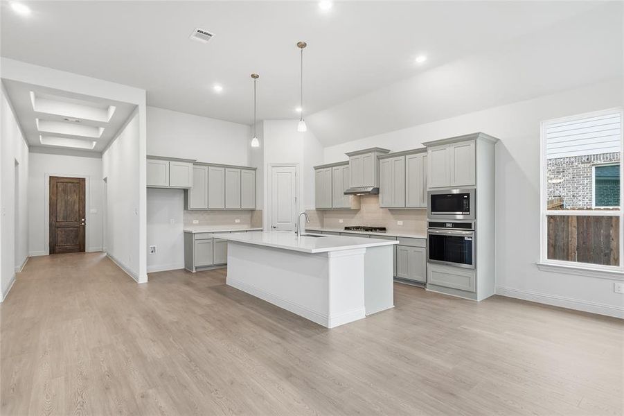 Kitchen with tasteful backsplash, gray cabinets, stainless steel appliances, an island with sink, and vaulted ceiling