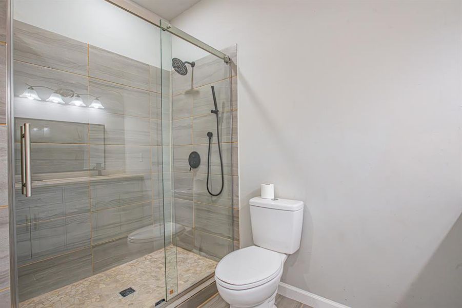 Full bath featuring toilet, baseboards, and a stall shower