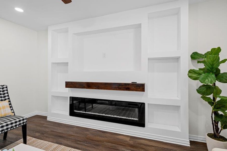 Living room featuring built in shelves, a glass covered fireplace, dark wood-style floors, and recessed lighting Living room featuring built in shelves, a glass covered fireplace, dark wood-style floors, and recessed lighting