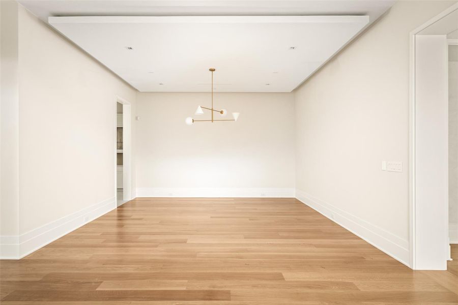A refined dining space defined by clean lines, a tray ceiling with subtle cove lighting, and a sculptural designer fixture - offering a neutral canvas ready to be personalized