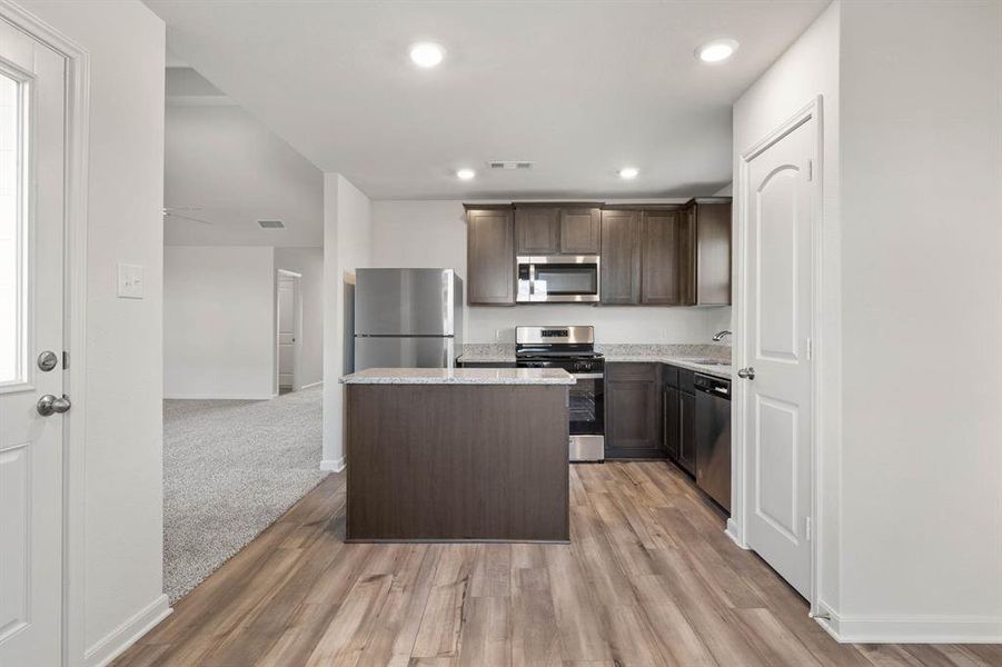 Kitchen with dark brown cabinets, stainless steel appliances, light wood-type flooring, sink, and a kitchen island