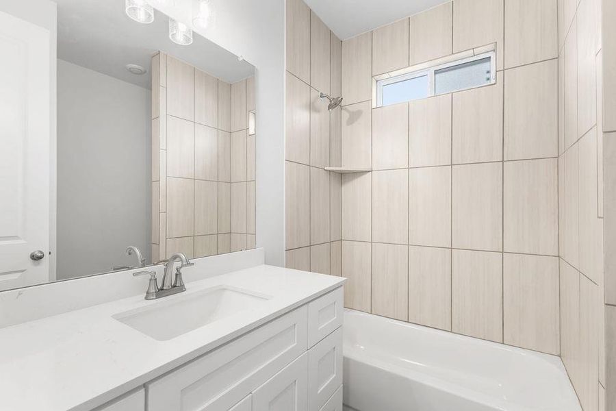 A well-lit bathroom features a white vanity, a large mirror, and tiled shower surround with a built-in shelf. A well-lit bathroom features a white vanity, a large mirror, and tiled shower surround with a built-in shelf.