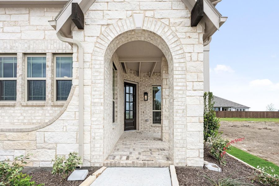 Home entrance with large stone arch, black front door, and covered brick porch