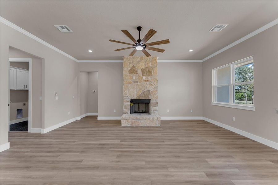 Unfurnished living room featuring a stone fireplace, crown molding, a ceiling fan, light wood-type flooring, and recessed lighting