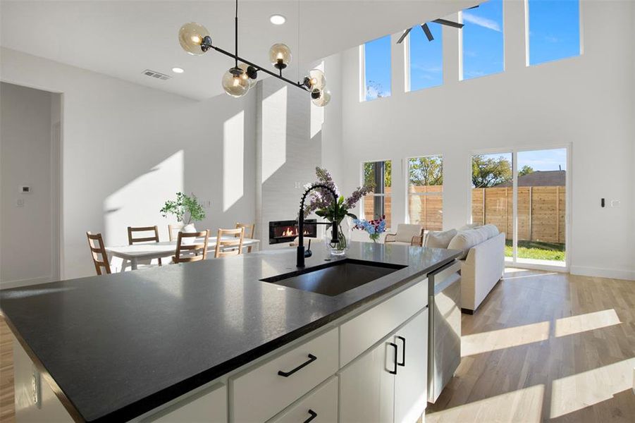 Kitchen featuring sink, an island with sink, a fireplace, white cabinets, and light wood-type flooring