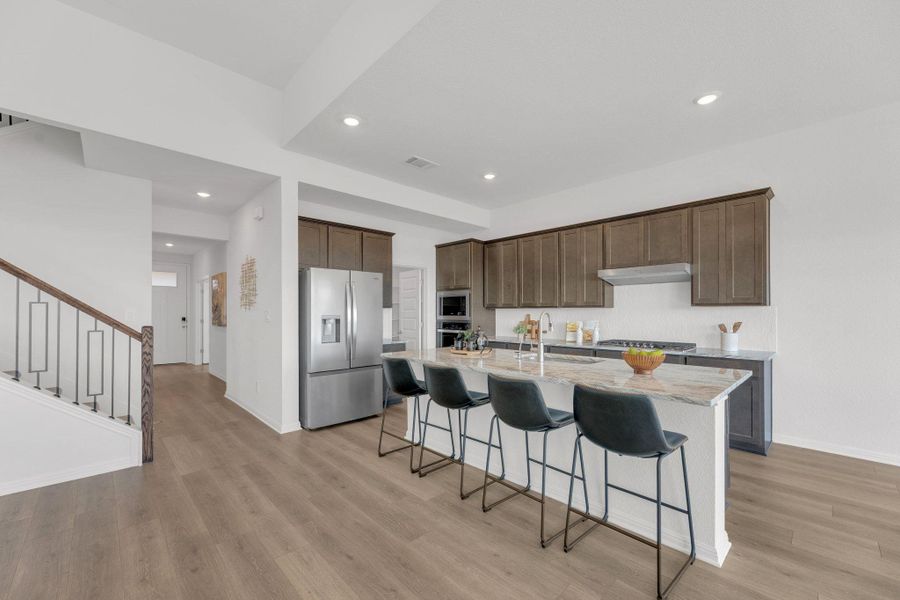 Kitchen with a breakfast bar, light stone counters, dark brown cabinetry, appliances with stainless steel finishes, and recessed lighting Kitchen with a breakfast bar, light stone counters, dark brown cabinetry, appliances with stainless steel finishes, and recessed lighting