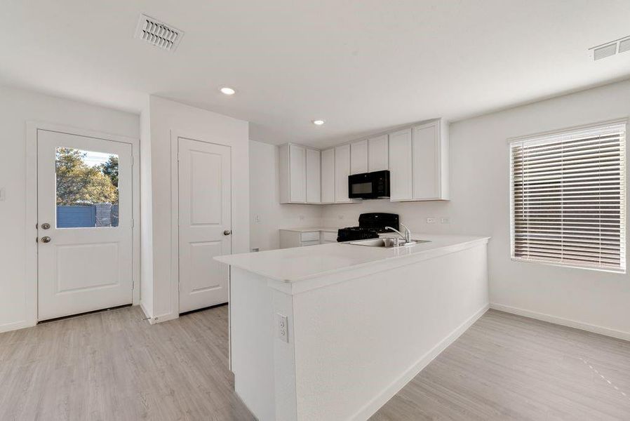 Kitchen featuring sink, stove, light hardwood / wood-style floors, white cabinets, and kitchen peninsula