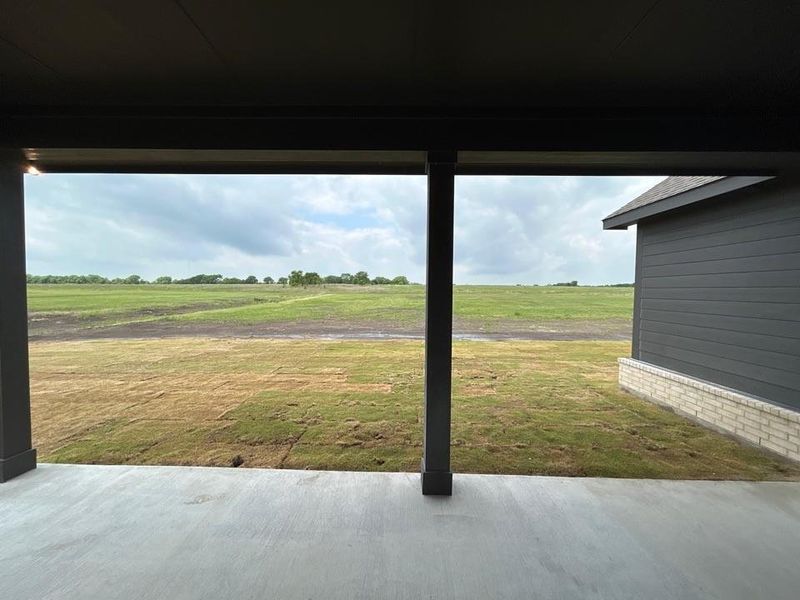 Covered concrete patio opening to an expansive green field