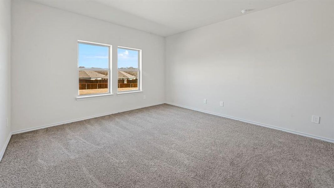 Spacious room featuring neutral carpeting, white walls, and two large windows with a neighborhood backdrop
