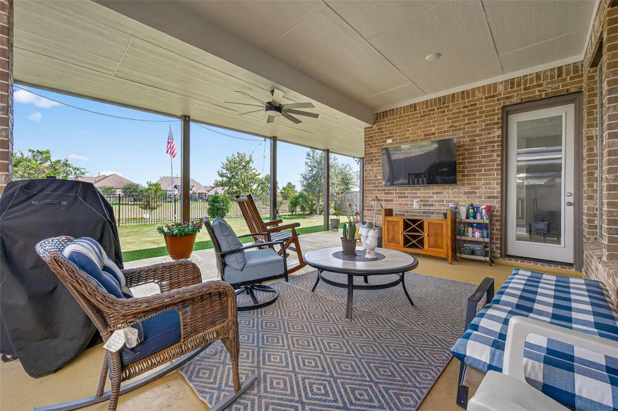 This inviting outdoor patio features a covered seating area with comfortable wicker furniture, a ceiling fan, and a mounted TV. It opens to a spacious backyard with a view, perfect for relaxation and entertaining. This inviting outdoor patio features a covered seating area with comfortable wicker furniture, a ceiling fan, and a mounted TV. It opens to a spacious backyard with a view, perfect for relaxation and entertaining.
