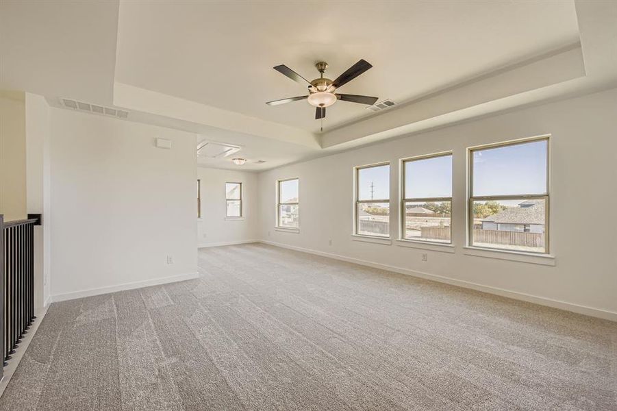 Empty room with a tray ceiling, light carpet, a ceiling fan, and attic access Empty room with a tray ceiling, light carpet, a ceiling fan, and attic access