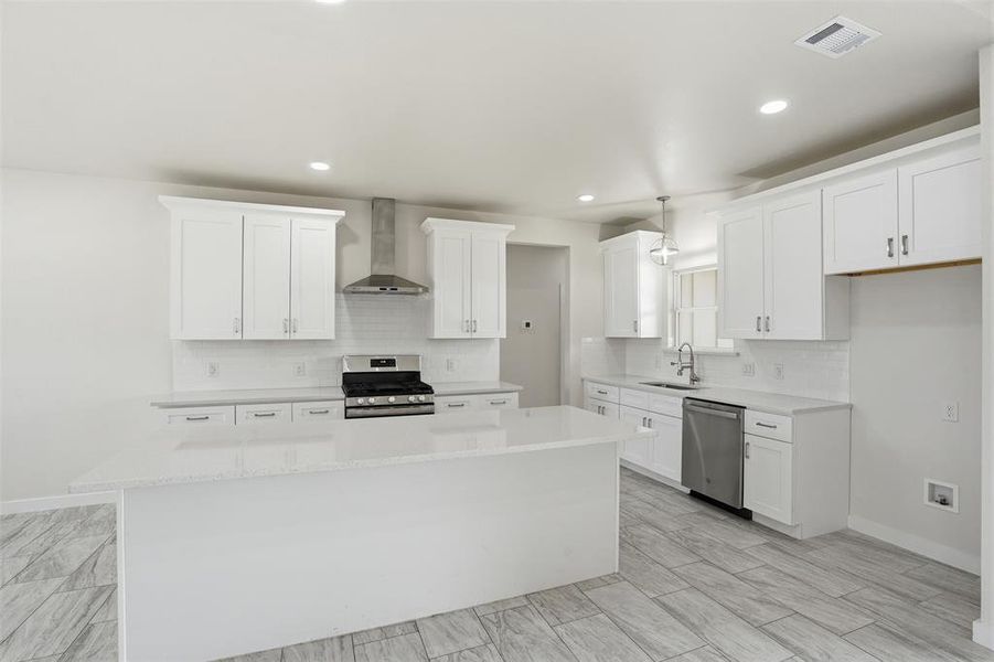 Bright kitchen featuring an island, white shaker cabinetry, stainless steel appliances, a subway tile backsplash, and light wood-finish flooring