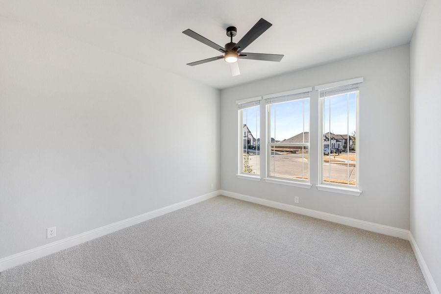 Empty bedroom with gray carpet, ceiling fan, and triple window overlooking neighborhood Empty bedroom with gray carpet, ceiling fan, and triple window overlooking neighborhood