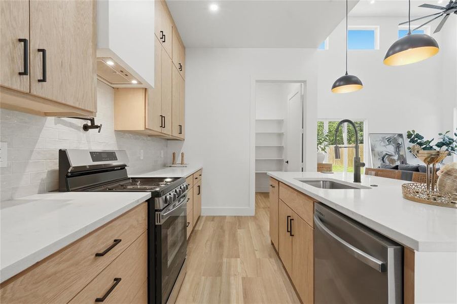 Modern kitchen featuring light wood-finish cabinetry, stainless steel appliances, a white tile backsplash, and a large central island with an undermount sink