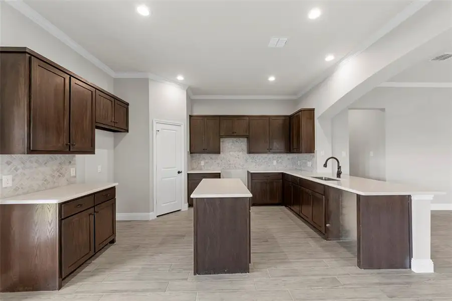 Kitchen with a peninsula, tasteful backsplash, a kitchen island, dark brown cabinets, and recessed lighting