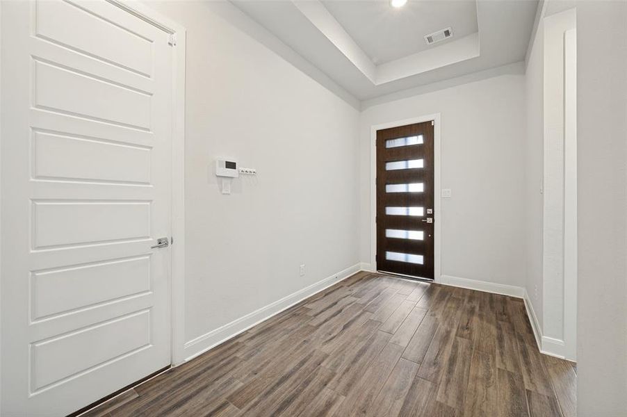 Entryway featuring wood-finish flooring, a contemporary dark wood entry door with frosted glass panels, a white five-panel interior door, and a tray ceiling with recessed lighting