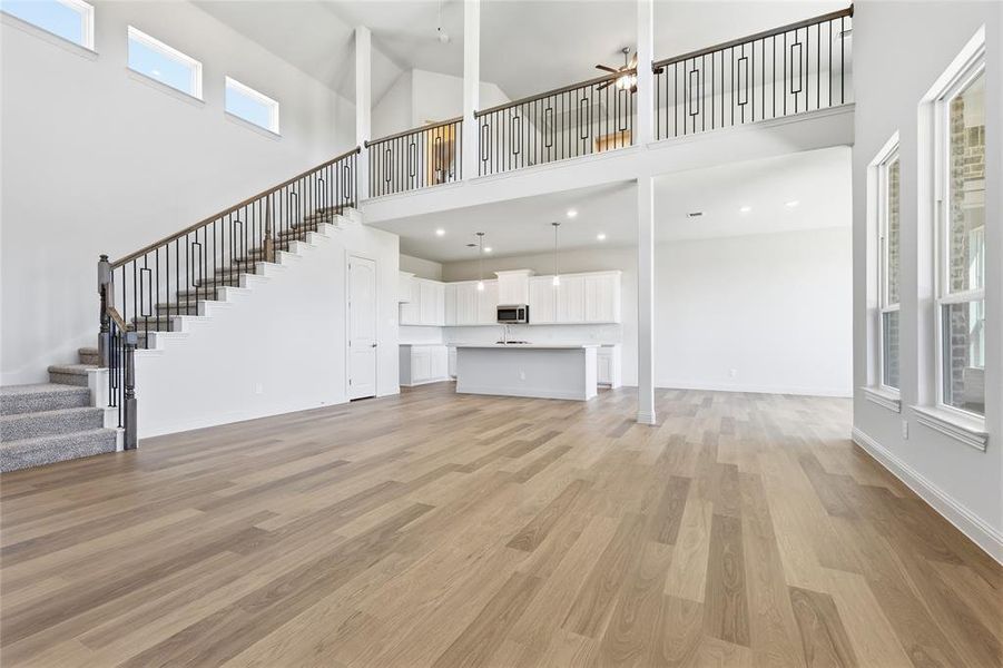 Unfurnished living room featuring light wood finished floors, ceiling fan, plenty of natural light, and a high ceiling