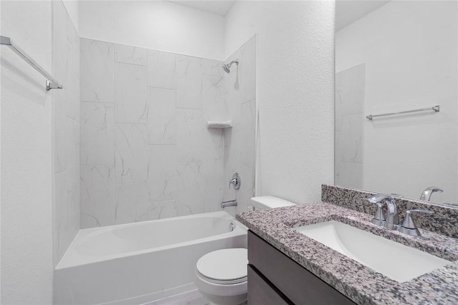 Secondary bathroom features granite countertops and stained cabinets, neutral paint, shower/tub combo with tile surround, large mirror, tile floors, and sleek fixtures and modern finishes.