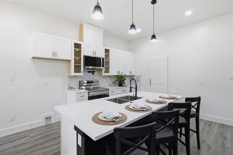 Modern kitchen featuring a large island with seating, white cabinetry, integrated stainless steel appliances, and wood-finish flooring