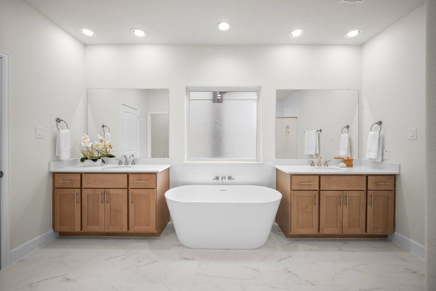 Dual vanities with quartz counters, warm wood cabinetry, marble-look tile floors, and a freestanding soaking tub centered between them — the primary bath is well-appointed with classic finishes. Dual vanities with quartz counters, warm wood cabinetry, marble-look tile floors, and a freestanding soaking tub centered between them — the primary bath is well-appointed with classic finishes.