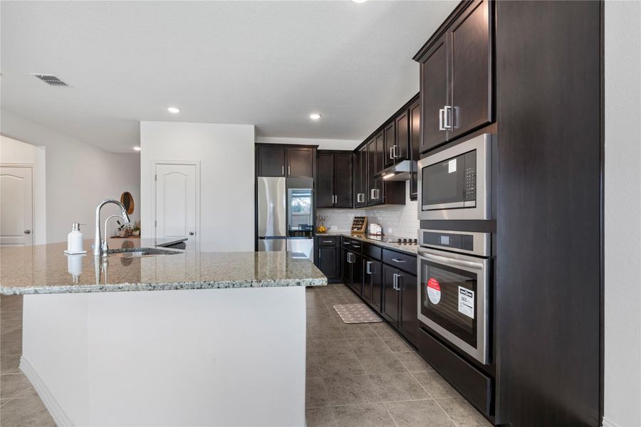 A contemporary kitchen features dark cabinetry, granite countertops, stainless steel appliances, and a central island. A contemporary kitchen features dark cabinetry, granite countertops, stainless steel appliances, and a central island.