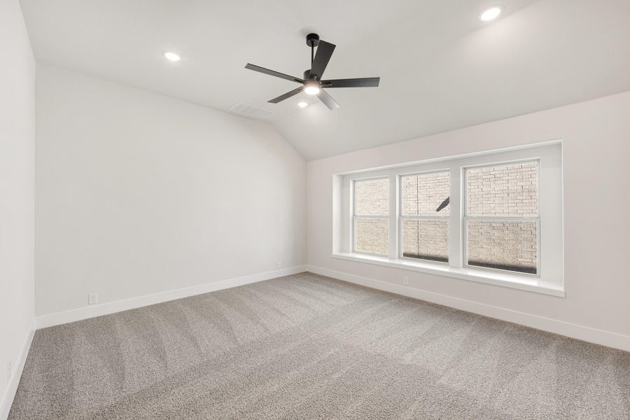 Empty bedroom with vaulted ceiling, black ceiling fan, gray carpet, and triple window with white trim