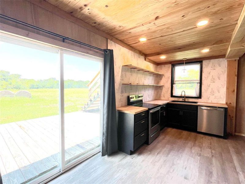 Kitchen with appliances with stainless steel finishes, dark cabinets, open shelves, and vinyl plank flooring