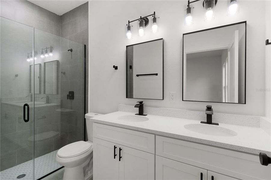 Primary bathroom with tiled shower, dual sinks, and frameless glass shower door