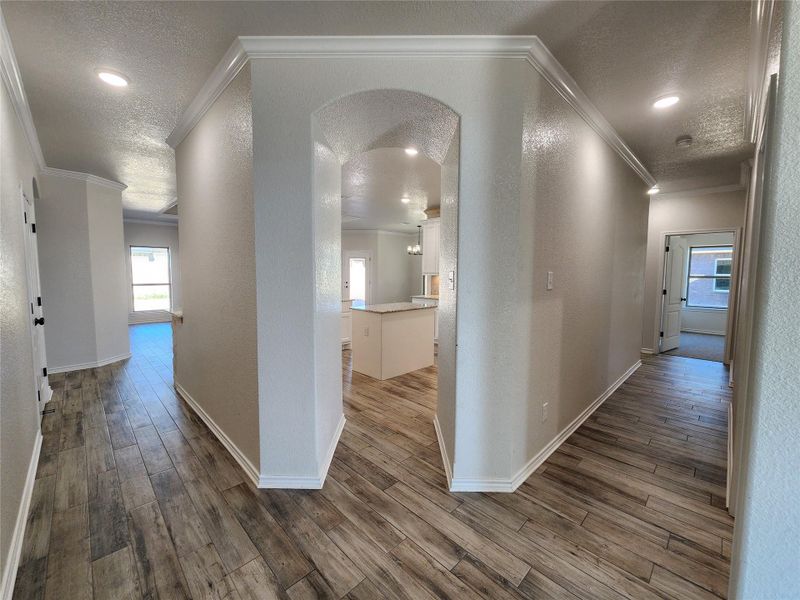 Corridor featuring arched walkways, wood finished floors, a textured ceiling, a textured wall, and recessed lighting