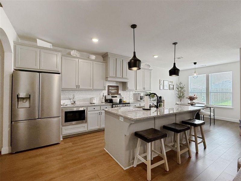 Kitchen with appliances with stainless steel finishes, backsplash, light stone counters, a kitchen breakfast bar, and pendant lighting Kitchen with appliances with stainless steel finishes, backsplash, light stone counters, a kitchen breakfast bar, and pendant lighting