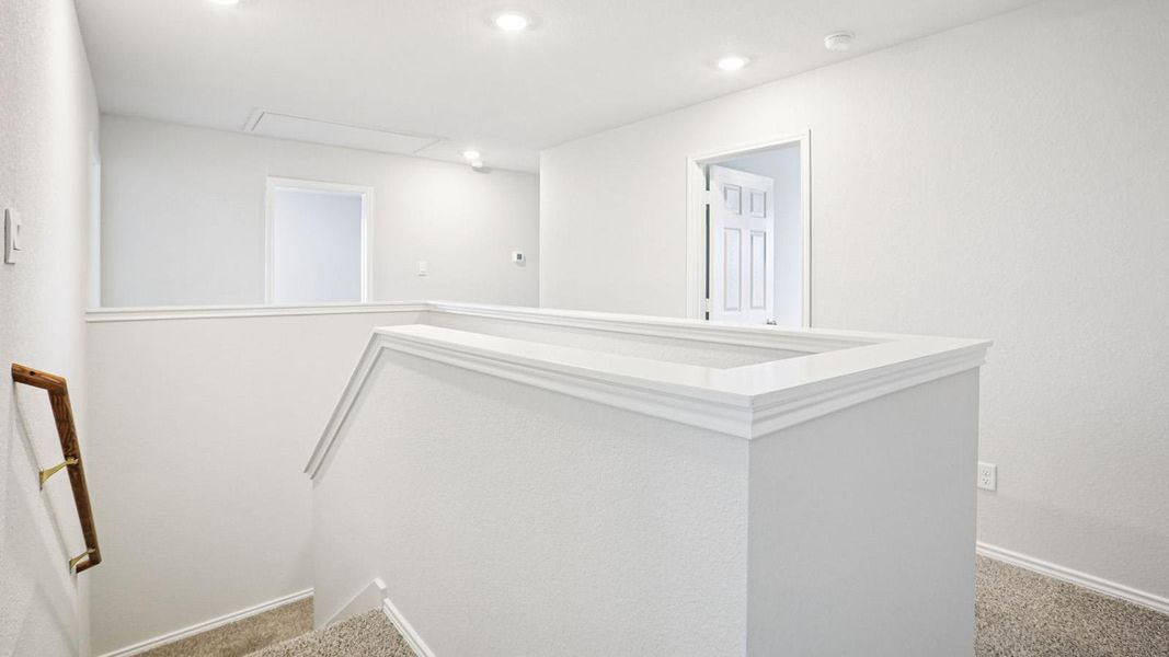 Upper-level landing featuring recessed lighting, a white painted half-wall with detailed cap molding, and a carpeted staircase with a wood handrail