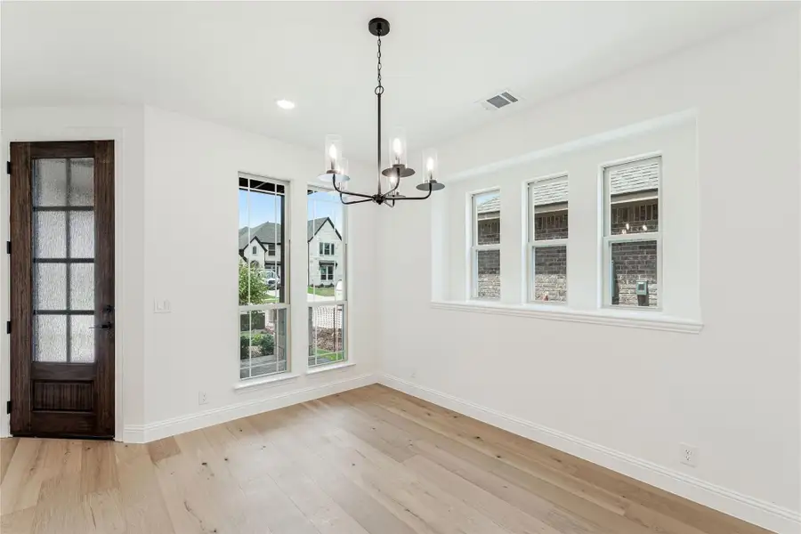 Empty dining room with hardwood floors, black chandelier, and large windows near a dark wood front door.