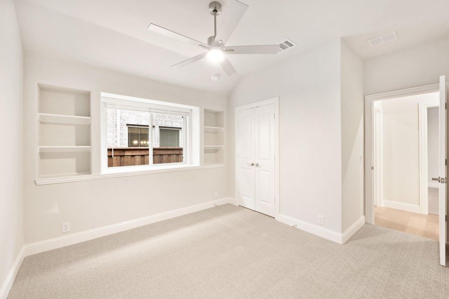 Empty bedroom with built-in shelves, ceiling fan, carpet flooring, and a closet door