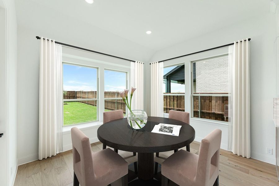 Bright dining nook with round dark wood table, four pink chairs, and large windows overlooking a fenced backyard