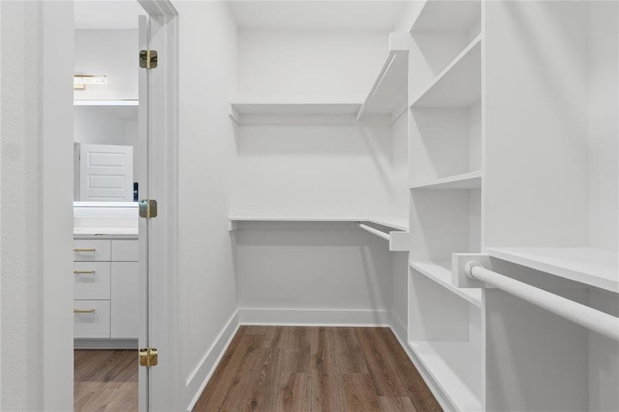 Walk-in closet featuring built-in shelving, multiple hanging rods, wood-finish flooring, white baseboards, and a white interior door