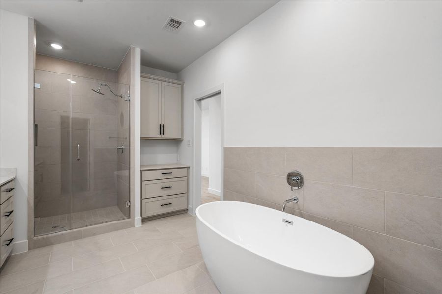 Primary bathroom oasis — freestanding soaking tub set against tile wainscoting, walk-in tile shower, and built-in storage drawers.