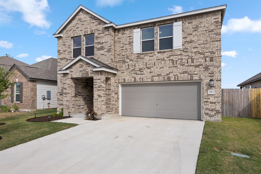 Traditional home featuring driveway, brick siding, and an attached garage