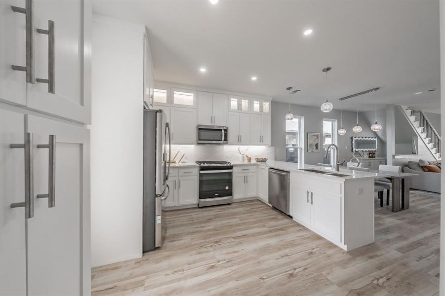 Kitchen featuring appliances with stainless steel finishes, pendant lighting, sink, white cabinets, and kitchen peninsula