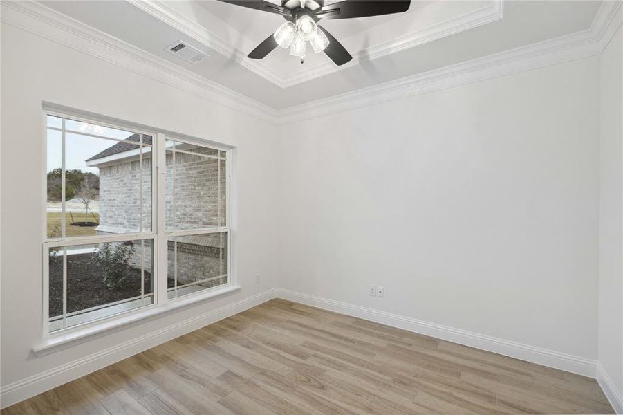 Unfurnished room with ceiling fan, a tray ceiling, ornamental molding, and light hardwood / wood-style flooring