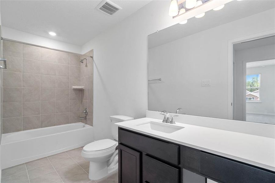 Secondary bath features tile flooring, bath/shower combo with tile surround, stained wood cabinets, beautiful light countertops, mirror, sleek fixtures and modern finishes.