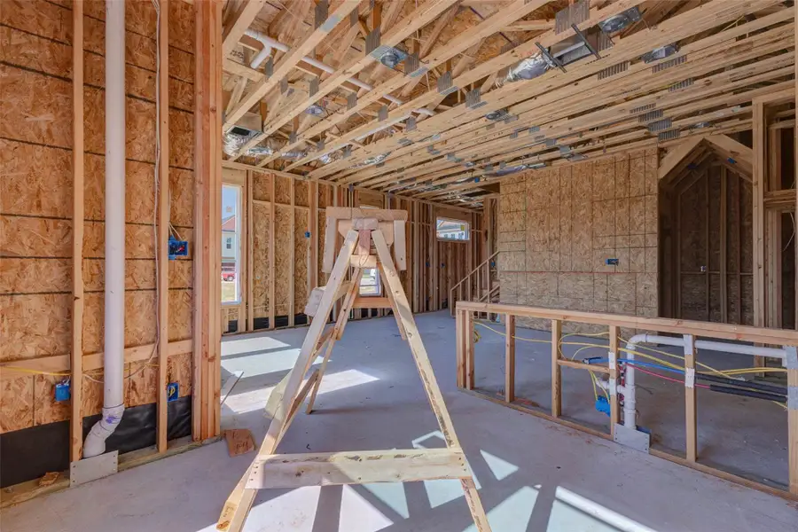Construction progress view of the kitchen and main living area, showing plumbing rough-ins, electrical work, framing, and ceiling systems in place. The open layout reveals how the future kitchen will connect to the surrounding living spaces, while the large windows and rear access help emphasize light, function, and indoor-outdoor flow. Construction progress view of the kitchen and main living area, showing plumbing rough-ins, electrical work, framing, and ceiling systems in place. The open layout reveals how the future kitchen will connect to the surrounding living spaces, while the large windows and rear access help emphasize light, function, and indoor-outdoor flow.