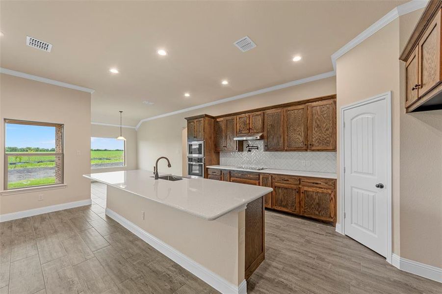 Kitchen featuring appliances with stainless steel finishes, ornamental molding, a sink, a center island with sink, and backsplash