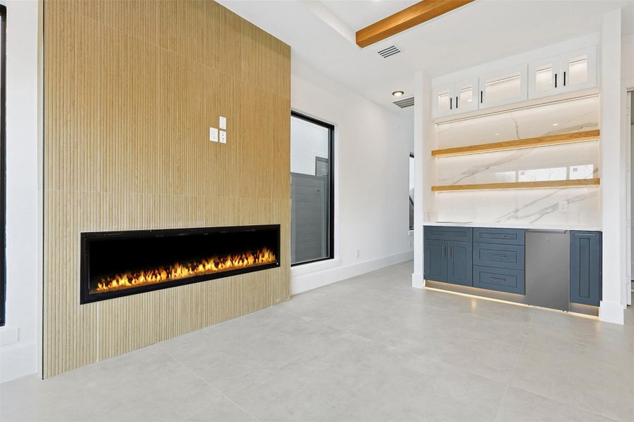 A wide linear fireplace is set within a floor-to-ceiling wood-slat feature wall, positioned next to a built-in wet bar with a wine fridge.