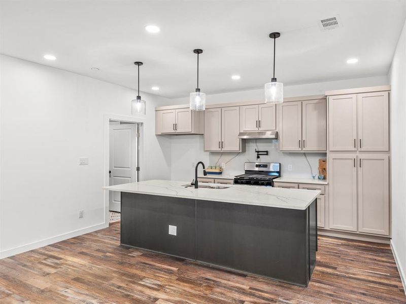 Kitchen featuring dark wood-style floors, hanging light fixtures, light stone counters, stainless steel gas stove, and recessed lighting